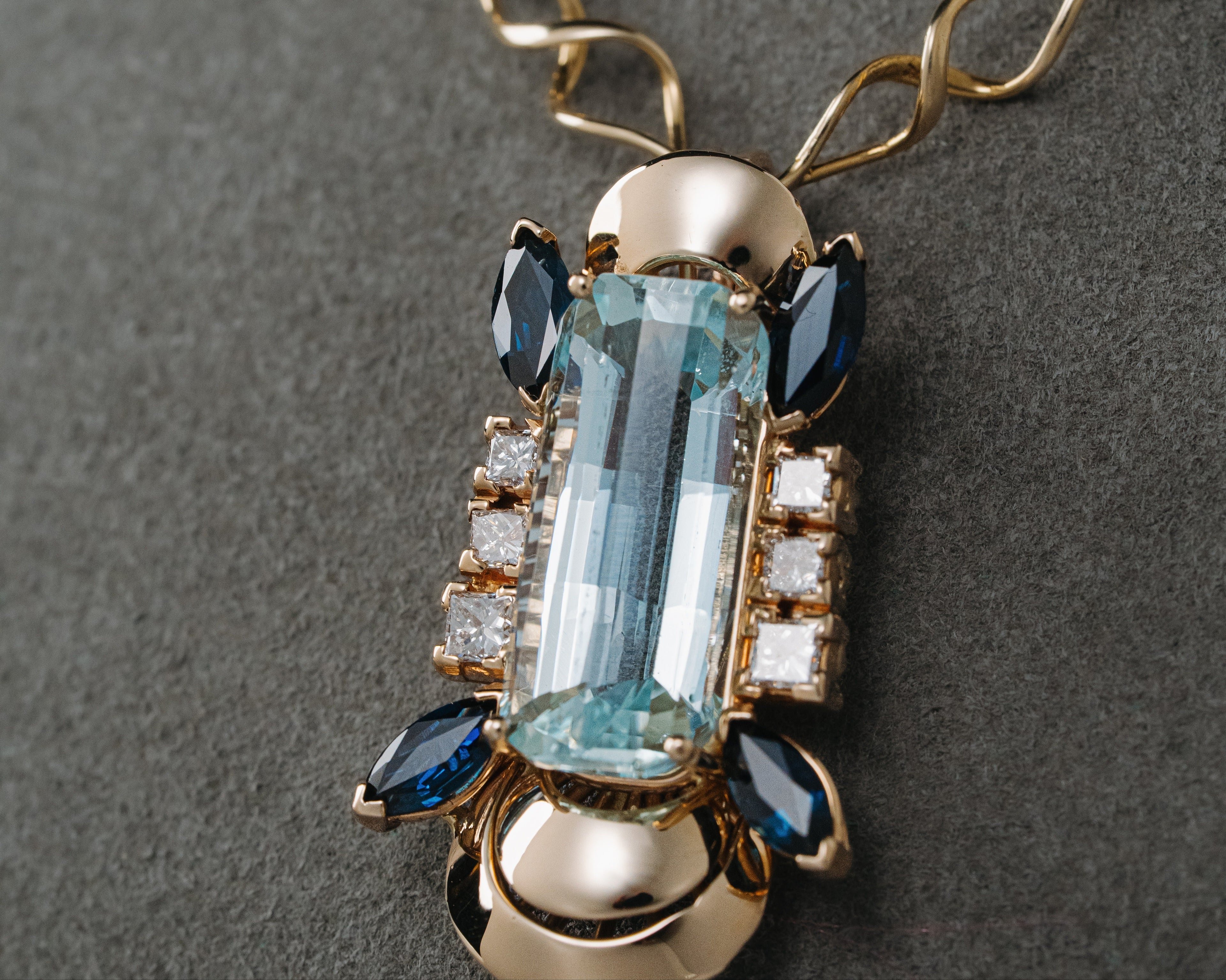 Gold necklace with a pendant featuring blue gemstones on a gray background