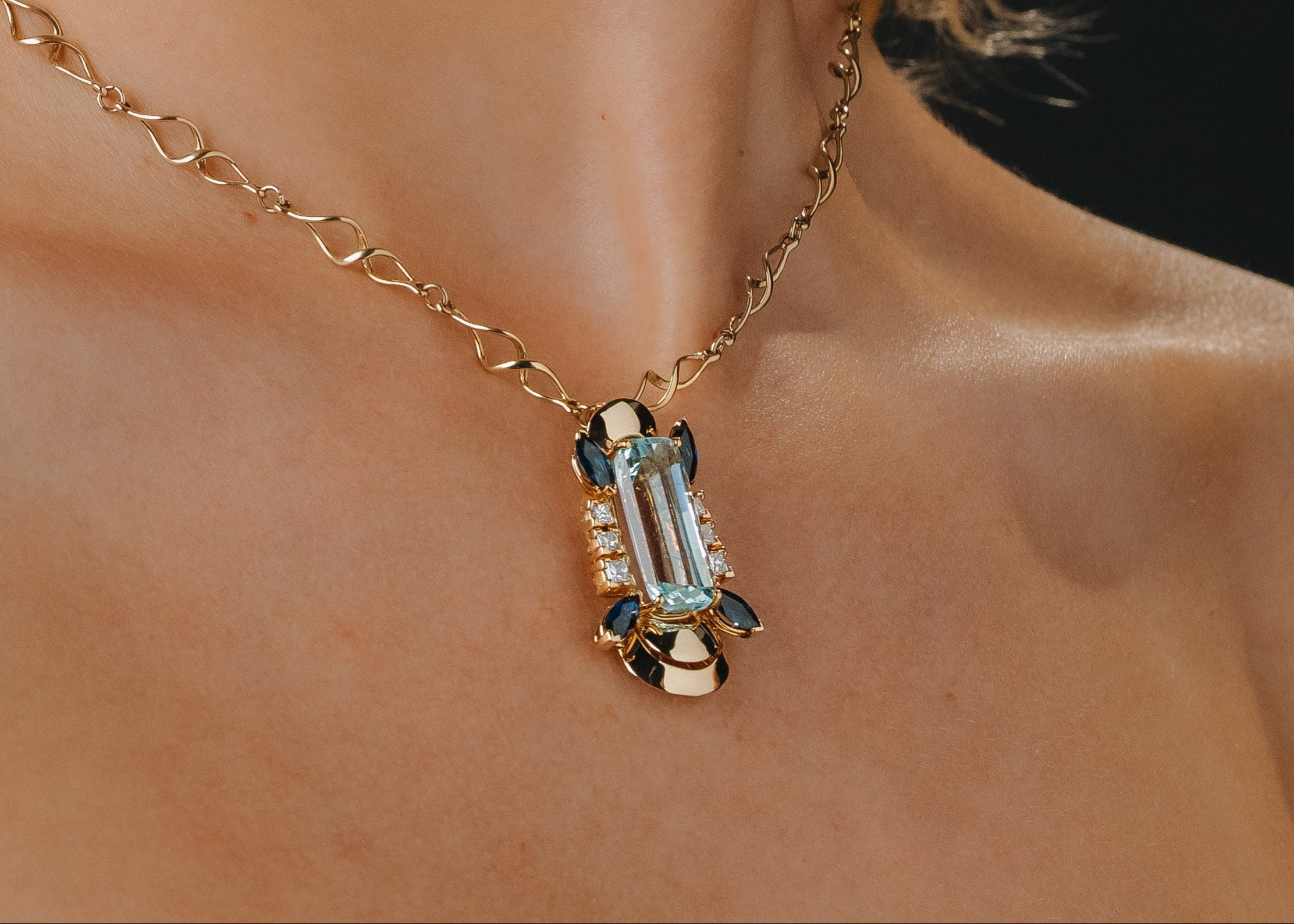 Woman wearing a gold necklace with a pendant against a black background